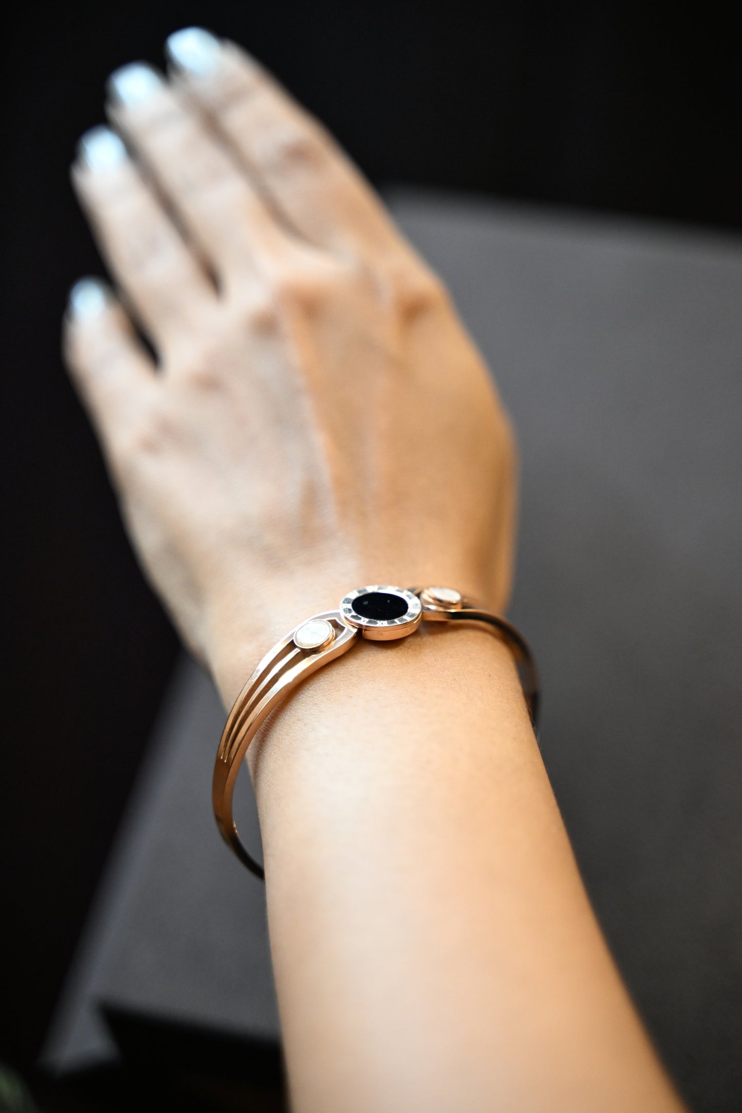 Close-up of a wrist wearing a bracelet with a dark central stone on a dark background