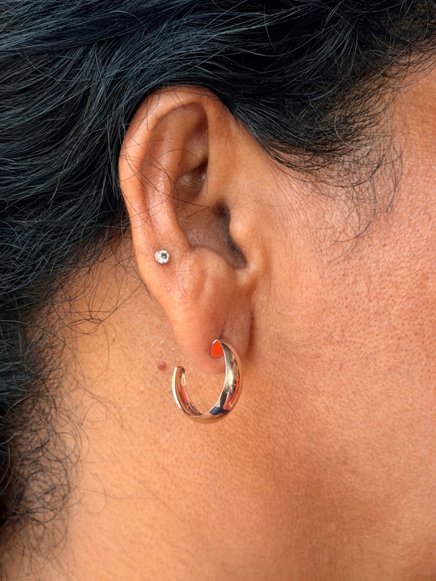 Close-up of an ear with a gold hoop earring and a small stud earring.